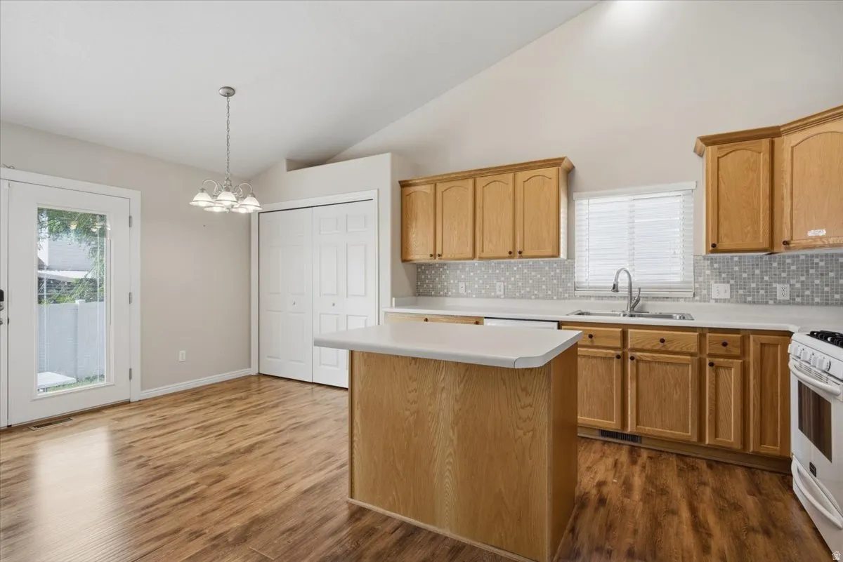 Kitchen featuring wood-finish flooring, vaulted ceiling, wood cabinetry, white countertops, and a tile backsplash