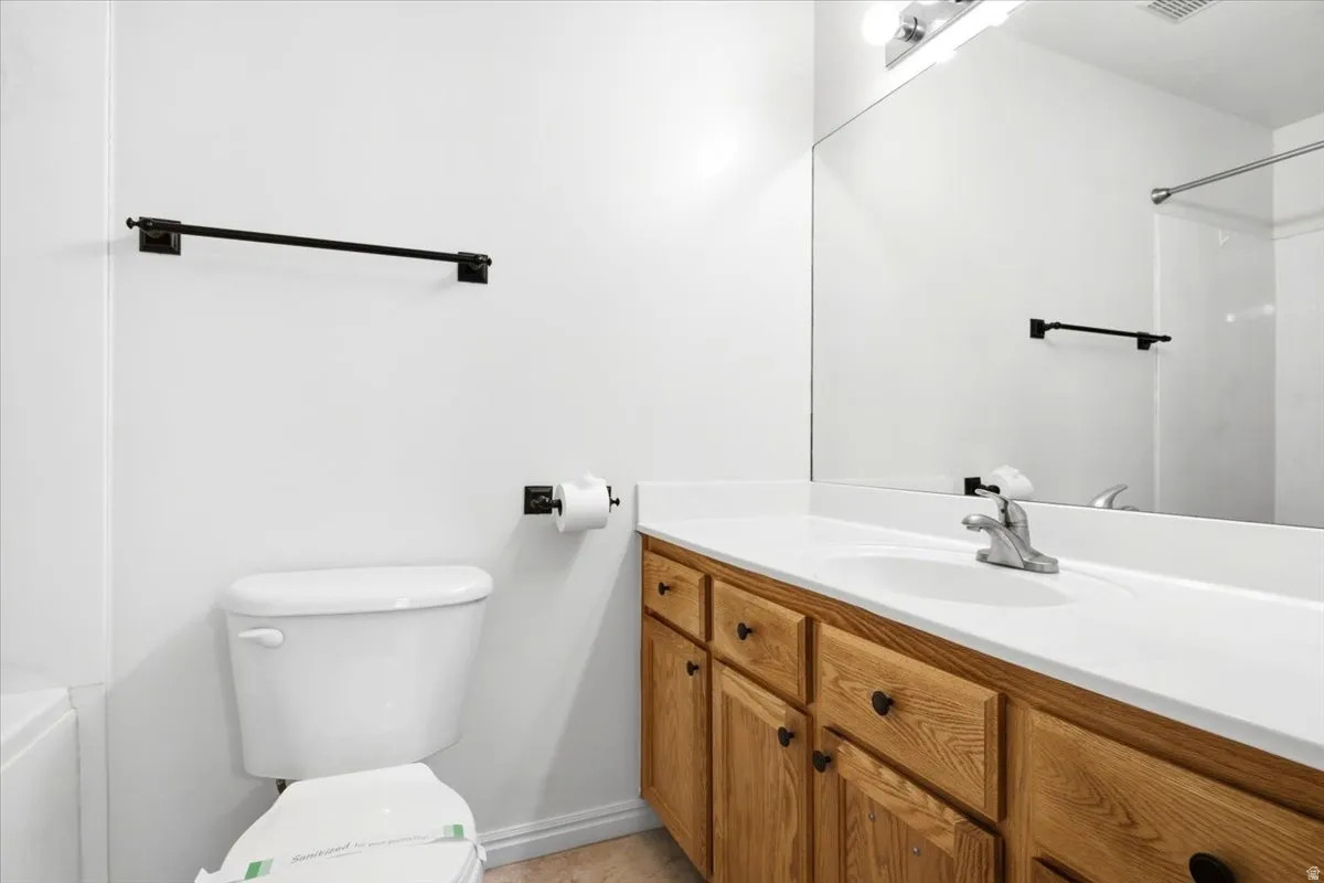 Bathroom featuring a wood-finish vanity with a white countertop and integrated sink, a large wall-mounted mirror, and a toilet