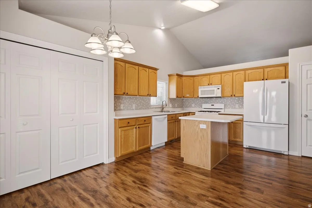Vaulted ceiling kitchen with wood-finish flooring, light wood cabinetry, white appliances, and a central island