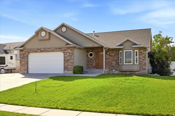 Stucco exterior with stone accent facade, attached garage with white door, wood entry door with circular window, bay window, and a gabled roof