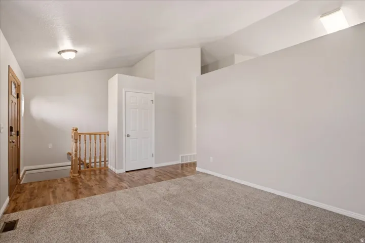 Vaulted ceiling with an overhead light fixture, light-toned carpeting, wood-finish flooring, and a natural wood staircase with balusters