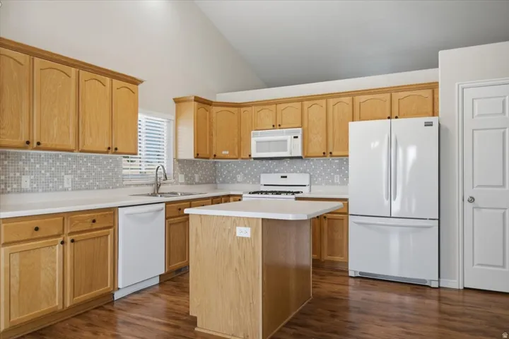 Kitchen featuring wood-finish cabinetry, light countertops, mosaic tile backsplash, a kitchen island, and wood-finish flooring