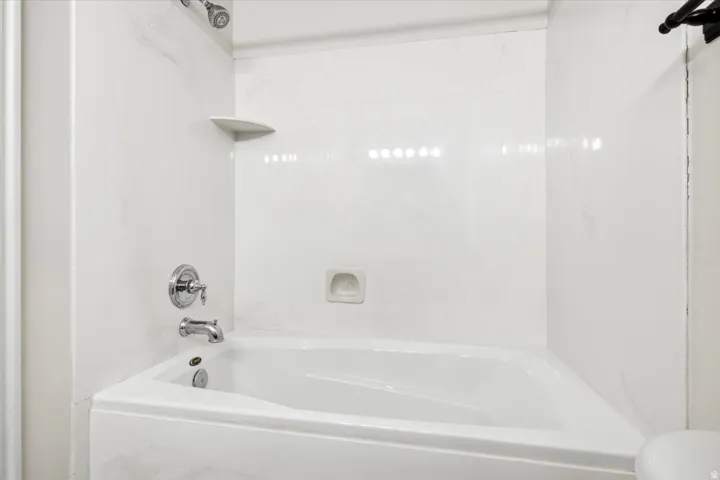 White bathtub with integrated shower, chrome fixtures, and a corner shelf