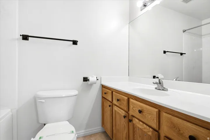 Bathroom featuring a wood-finish vanity with a white countertop and integrated sink, a large wall-mounted mirror, and a toilet
