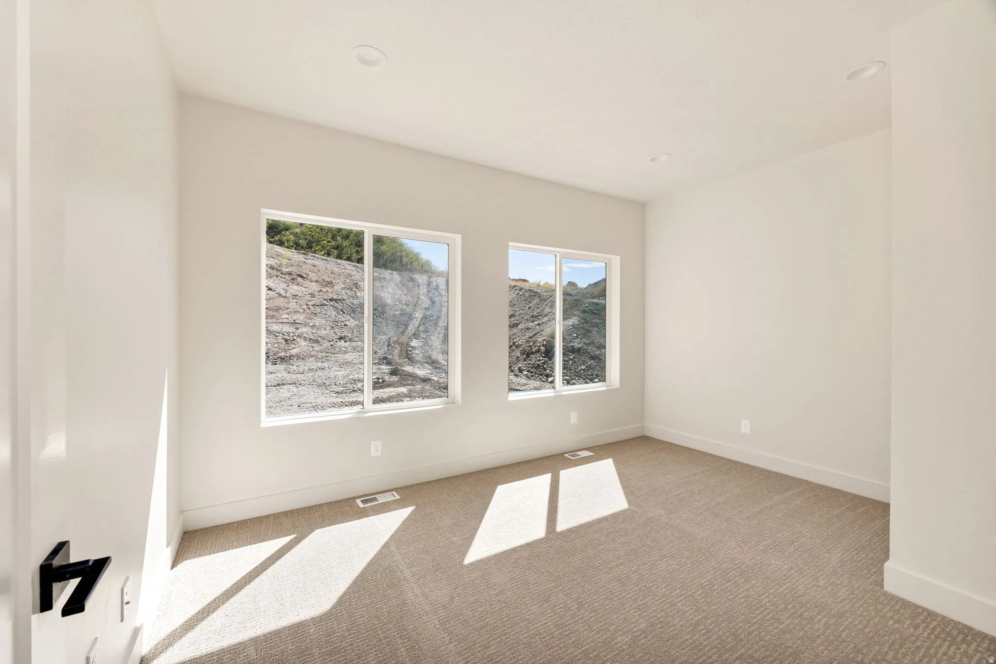 Recessed lighting, light neutral-toned walls, two large windows, and carpeted flooring
