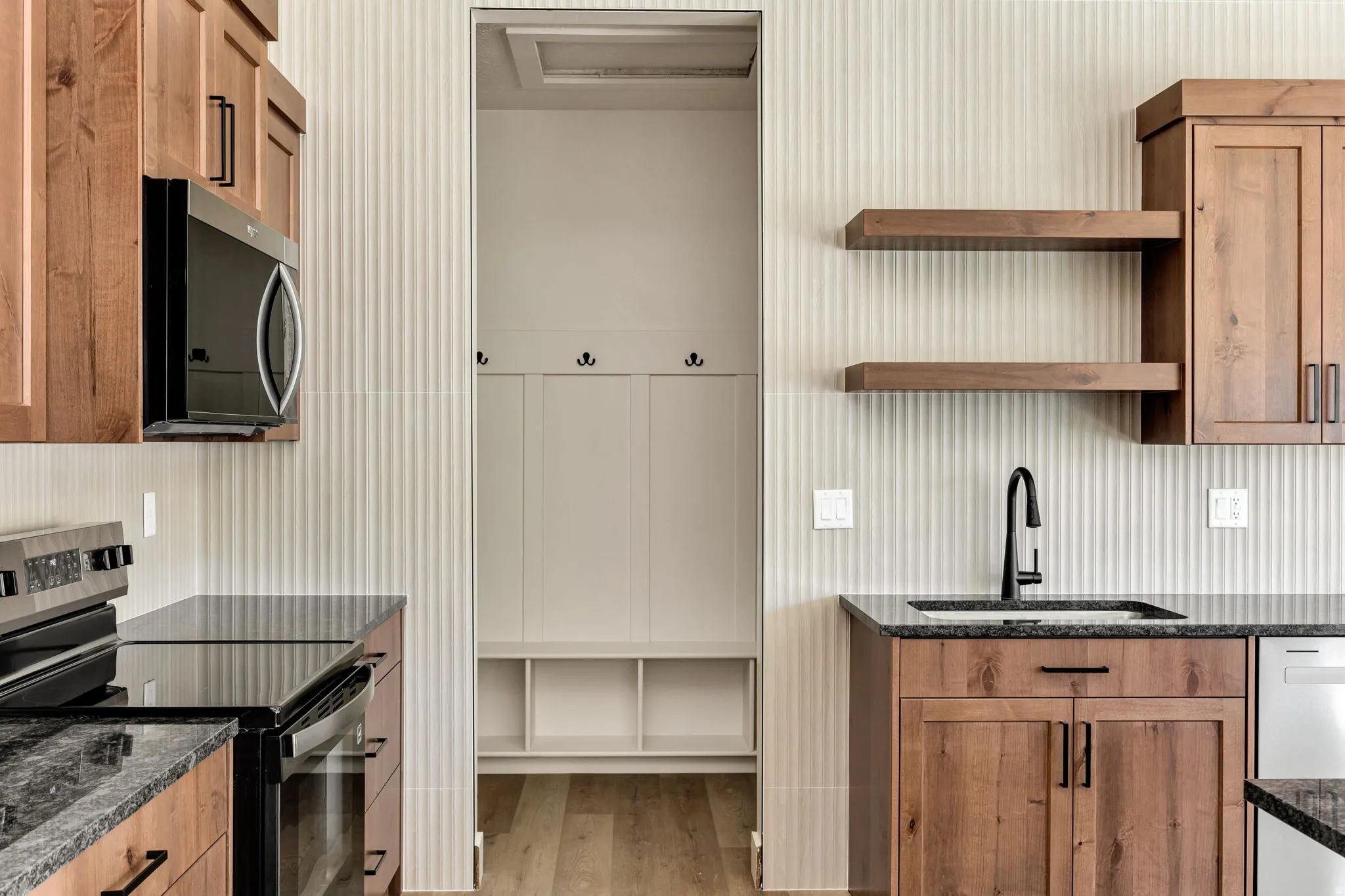 Wood-finish cabinetry, dark countertops, built-in microwave, and a black faucet at the sink