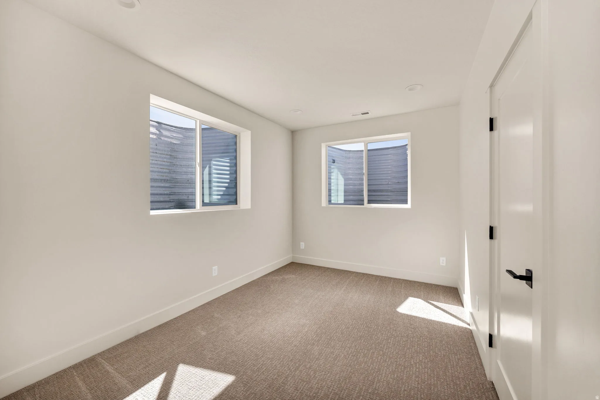Recessed ceiling lighting, two windows, wall-to-wall carpeting, white interior door with black hardware, and light-toned wall paint