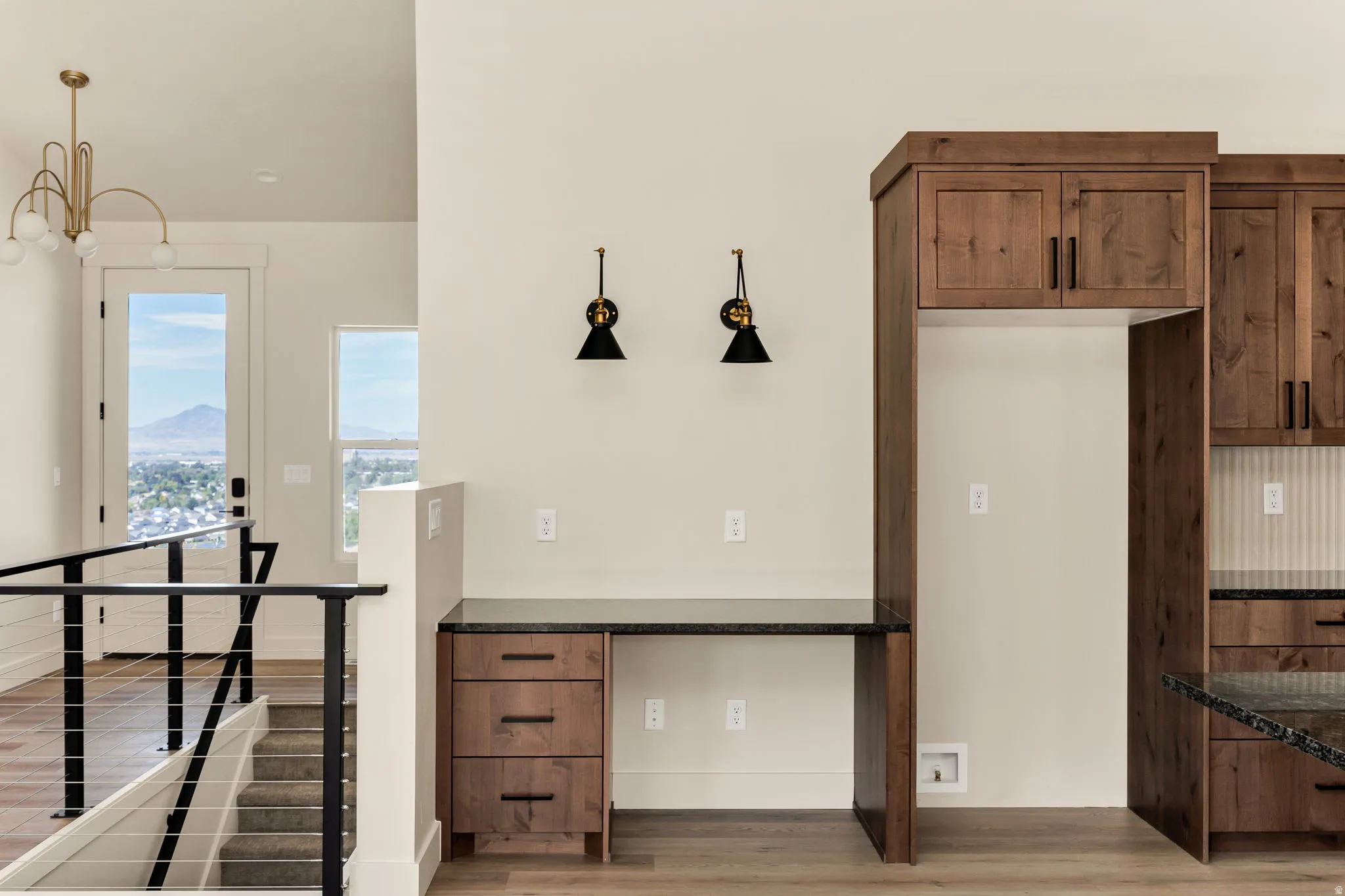 Built-in desk with dark countertop, integrated wood cabinetry, and sleek wall sconces