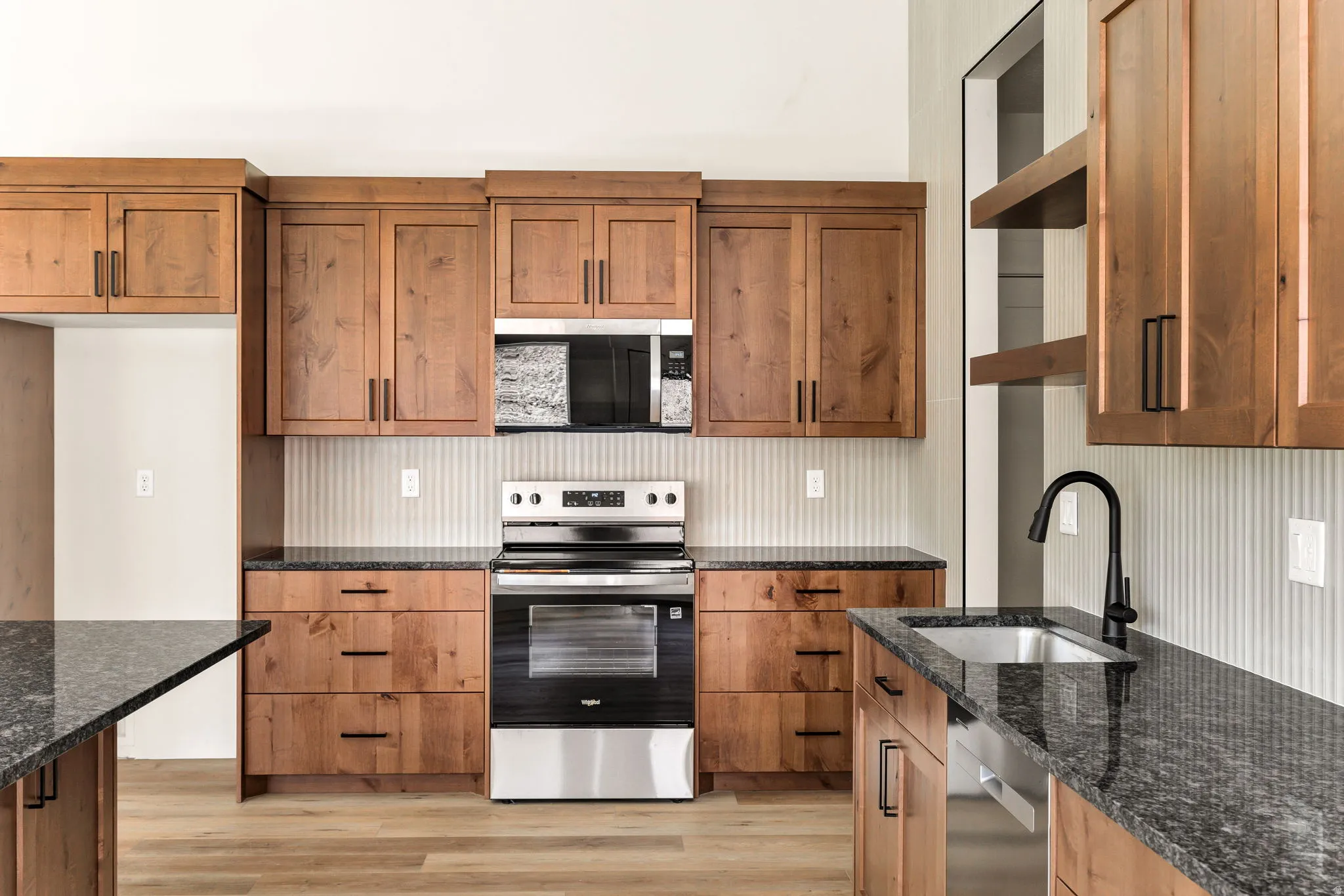 Kitchen featuring wood-finish cabinetry, dark countertops, stainless steel appliances, and a stainless steel sink with a matte black faucet