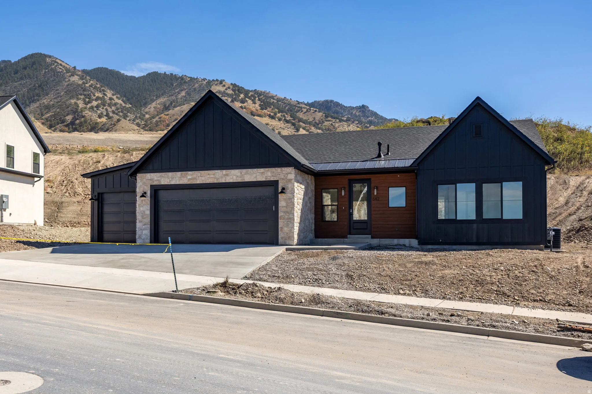 Modern exterior featuring black vertical siding, stone facade, a dark wood-tone accent wall, and multiple garage doors