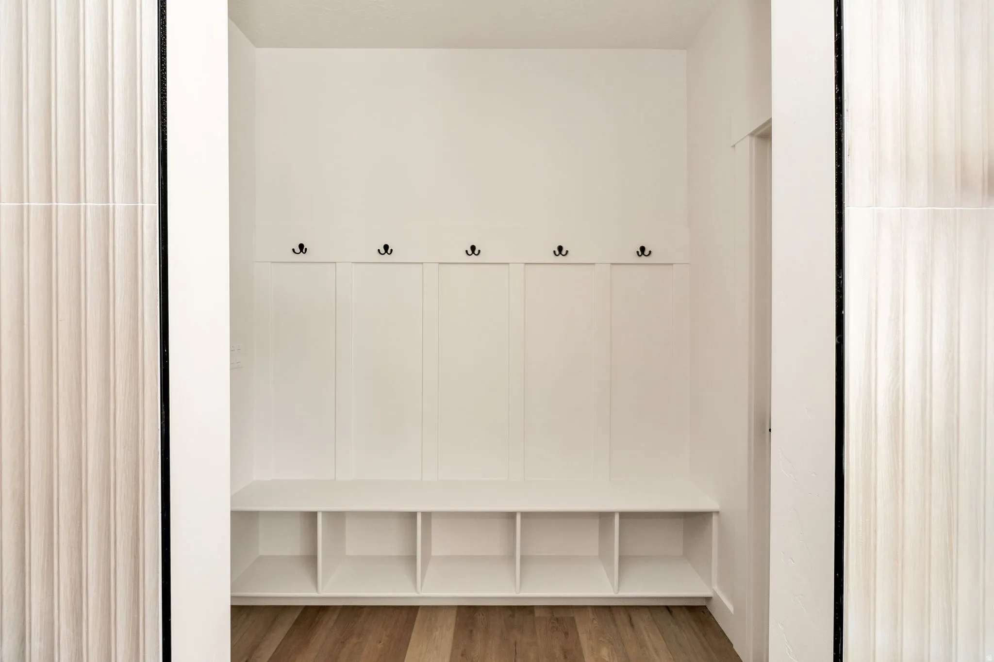 Built-in white storage bench with cubbies, five black hooks, and wood-finish flooring