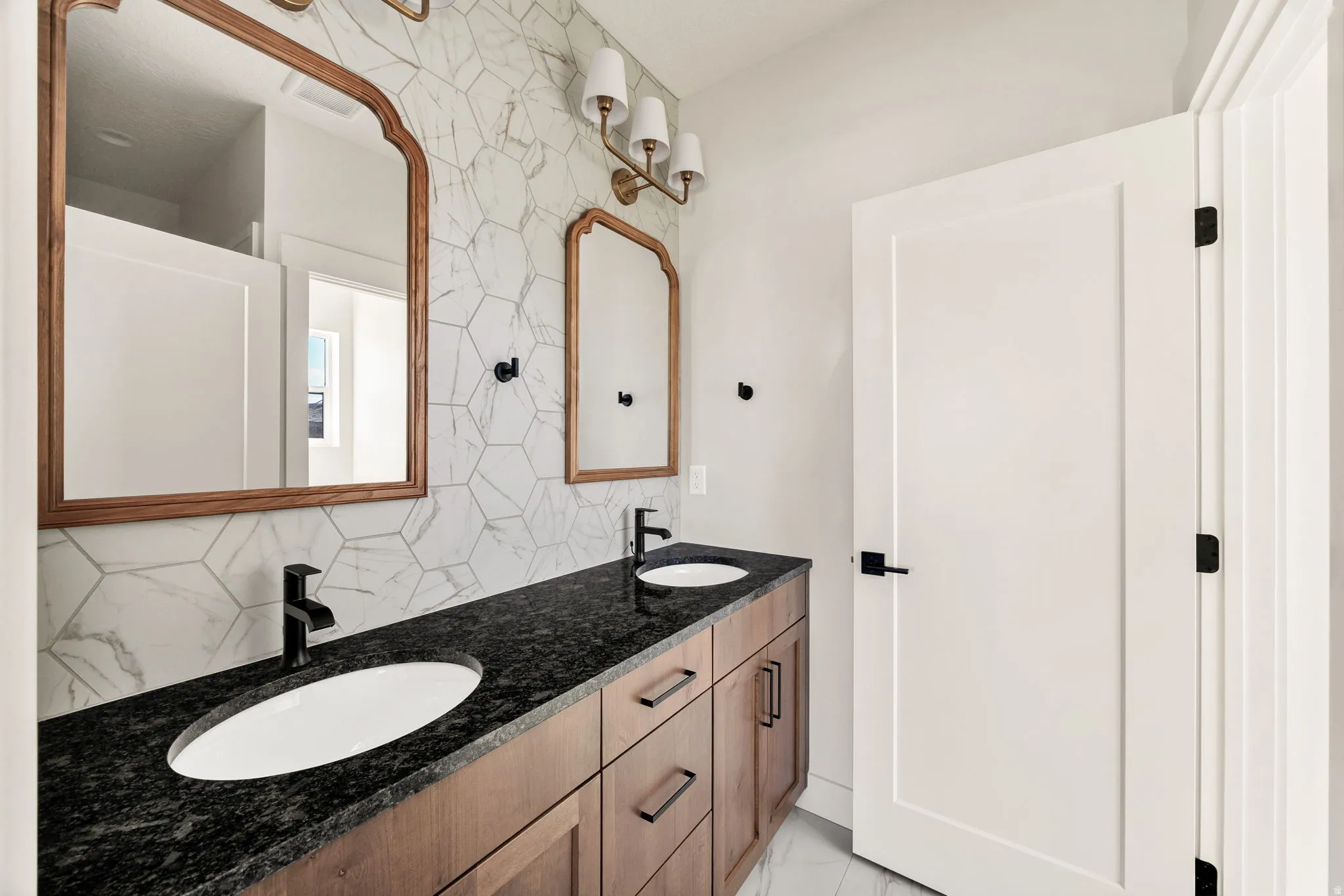 Dual vanity with wood-finish cabinetry, black stone countertop, and two undermount sinks
