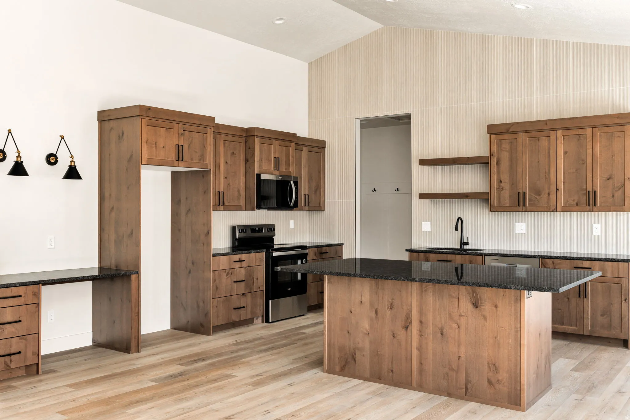 Vaulted ceiling with a white finish, wood-finish flooring, wood cabinetry with dark hardware, dark countertops, and a central island