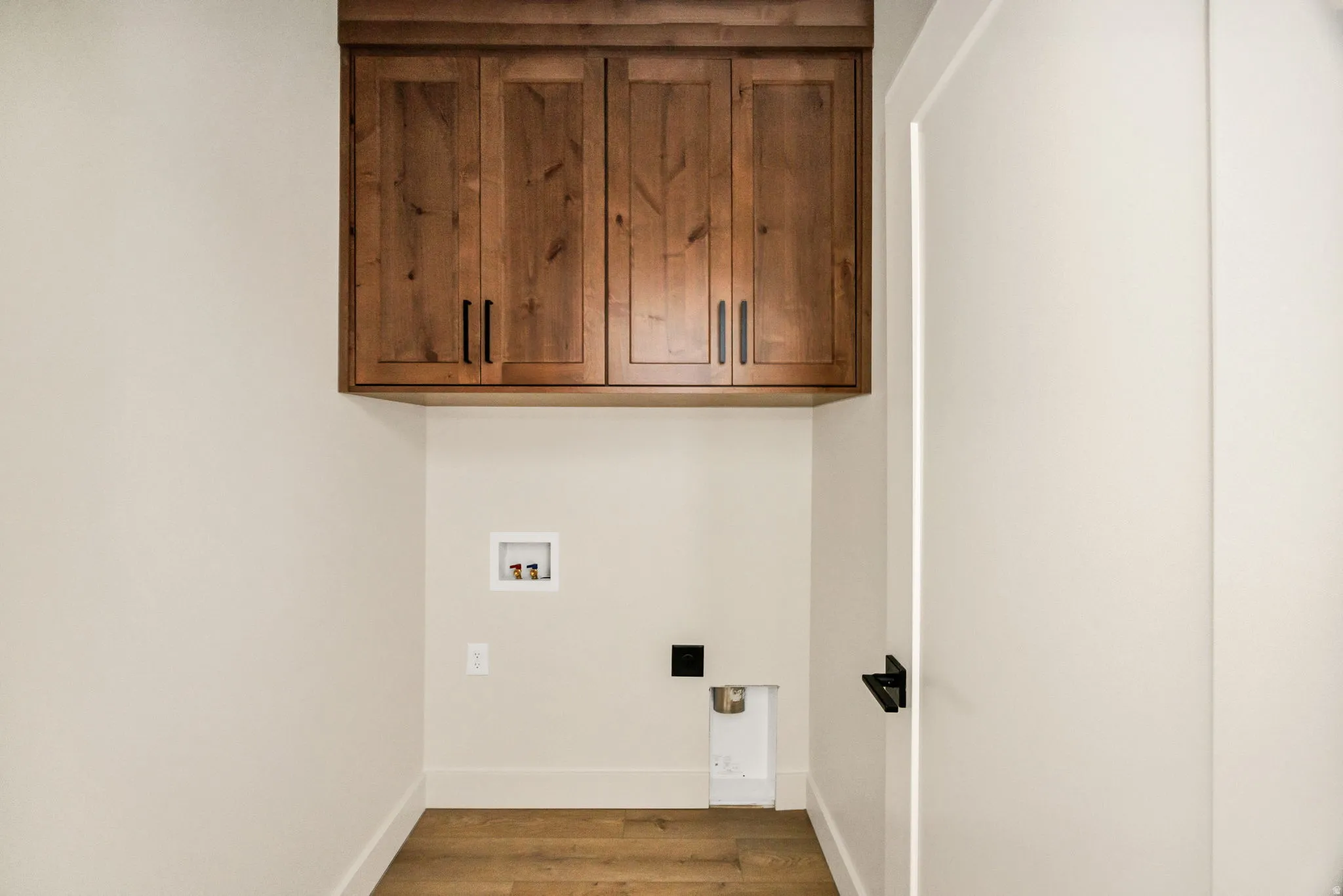 Wood-finish flooring, overhead wood cabinetry with matte black hardware, and a white interior door with matte black hardware