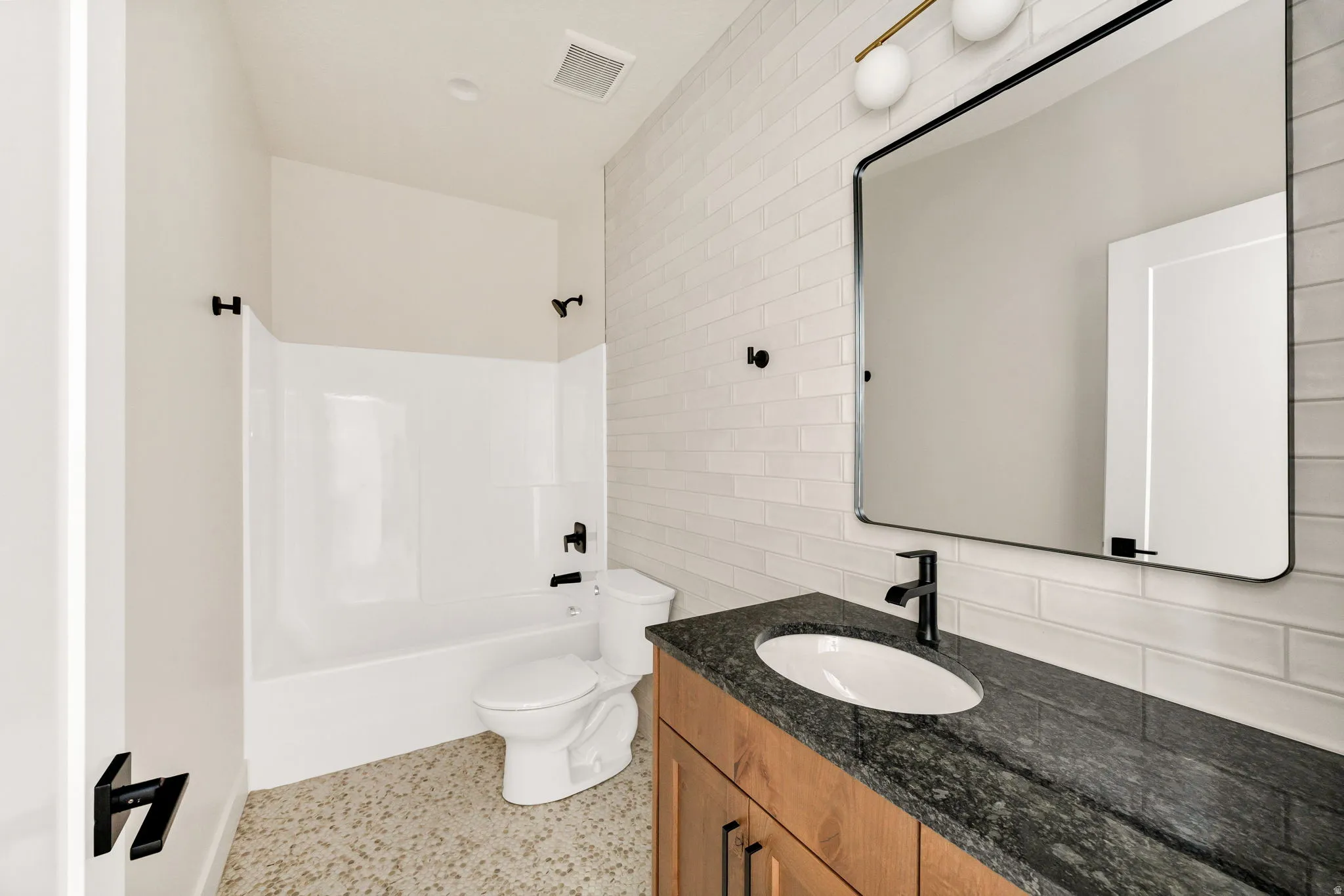 Wood-finish vanity with a dark countertop, undermount sink, and matte black faucet