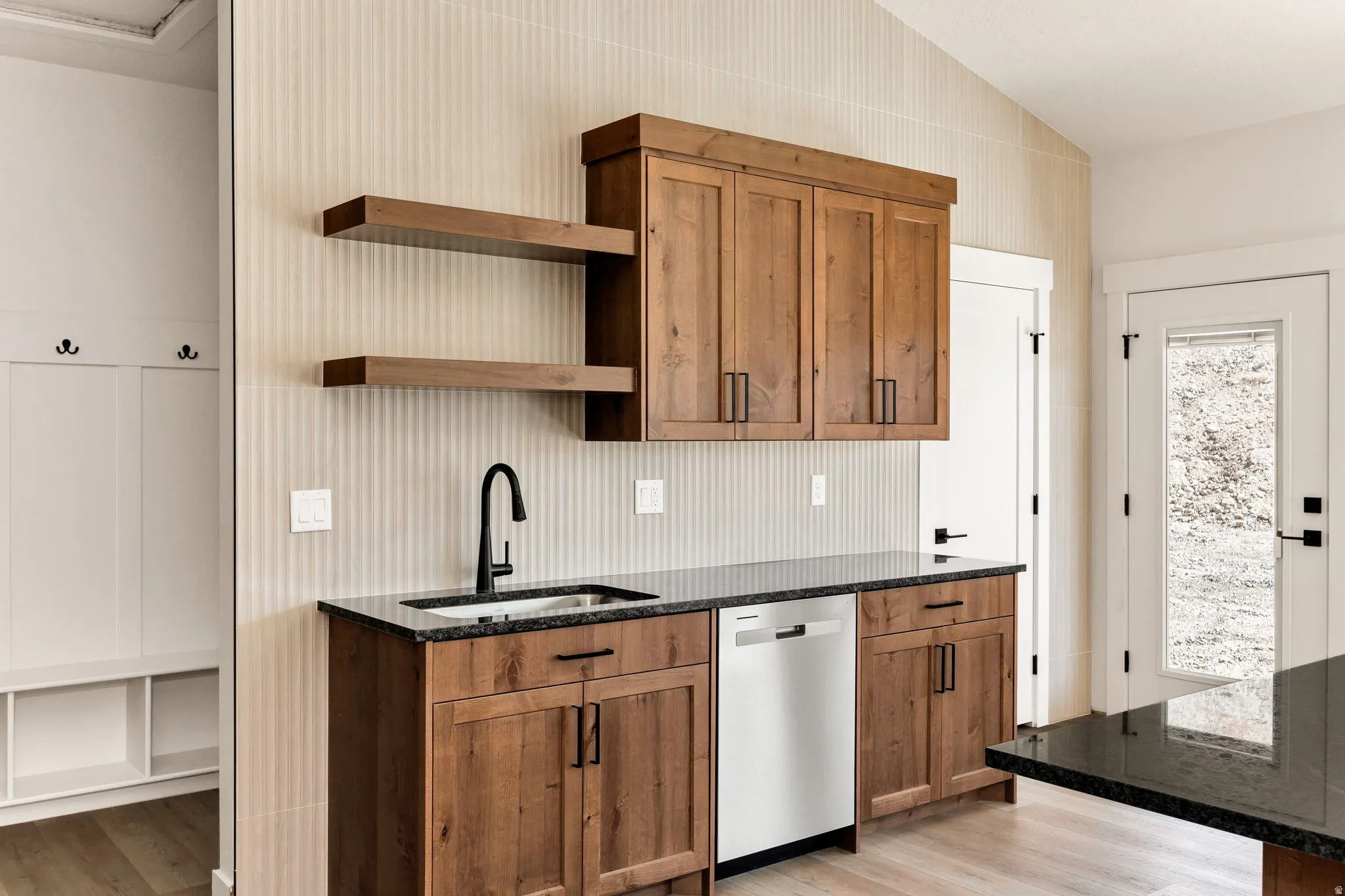 Built-in cabinetry with wood-finish doors, black hardware, black sink faucet, dark countertop, and built-in dishwasher