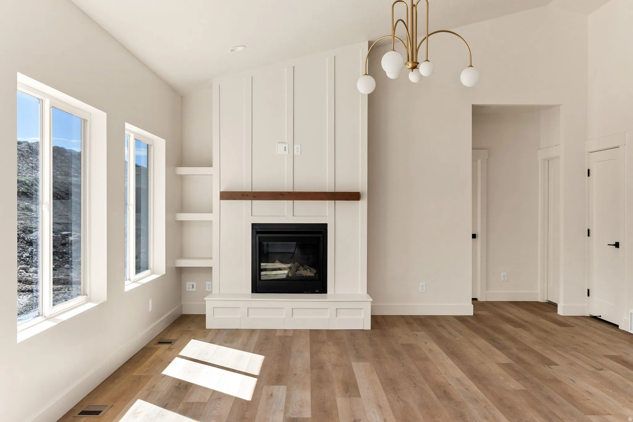 Vaulted ceiling, wood-finish flooring, built-in fireplace with wood mantel, integrated shelving, and a modern chandelier