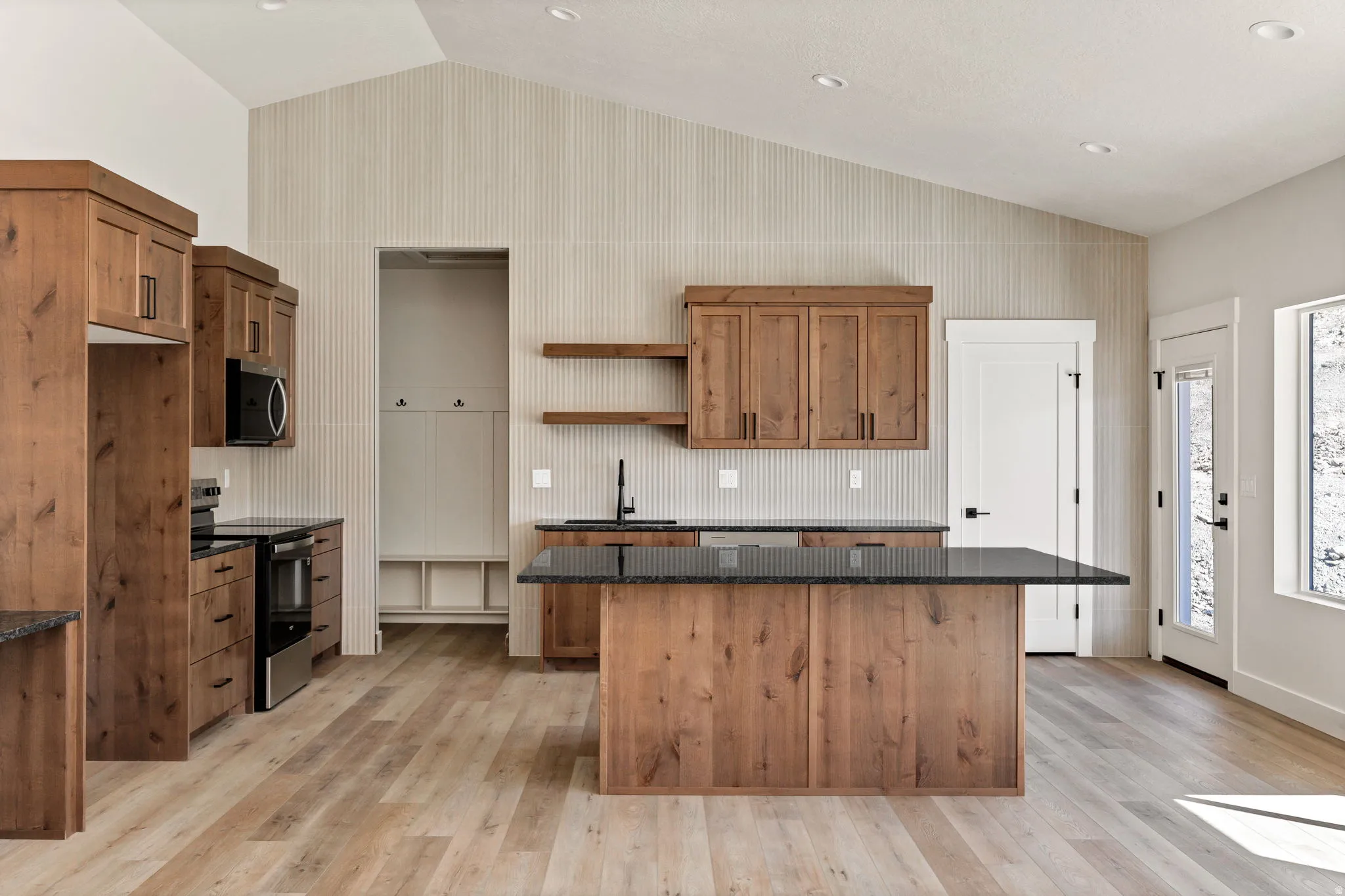 Wood-finish flooring, vaulted ceiling, wood cabinetry, dark countertops, and stainless steel appliances