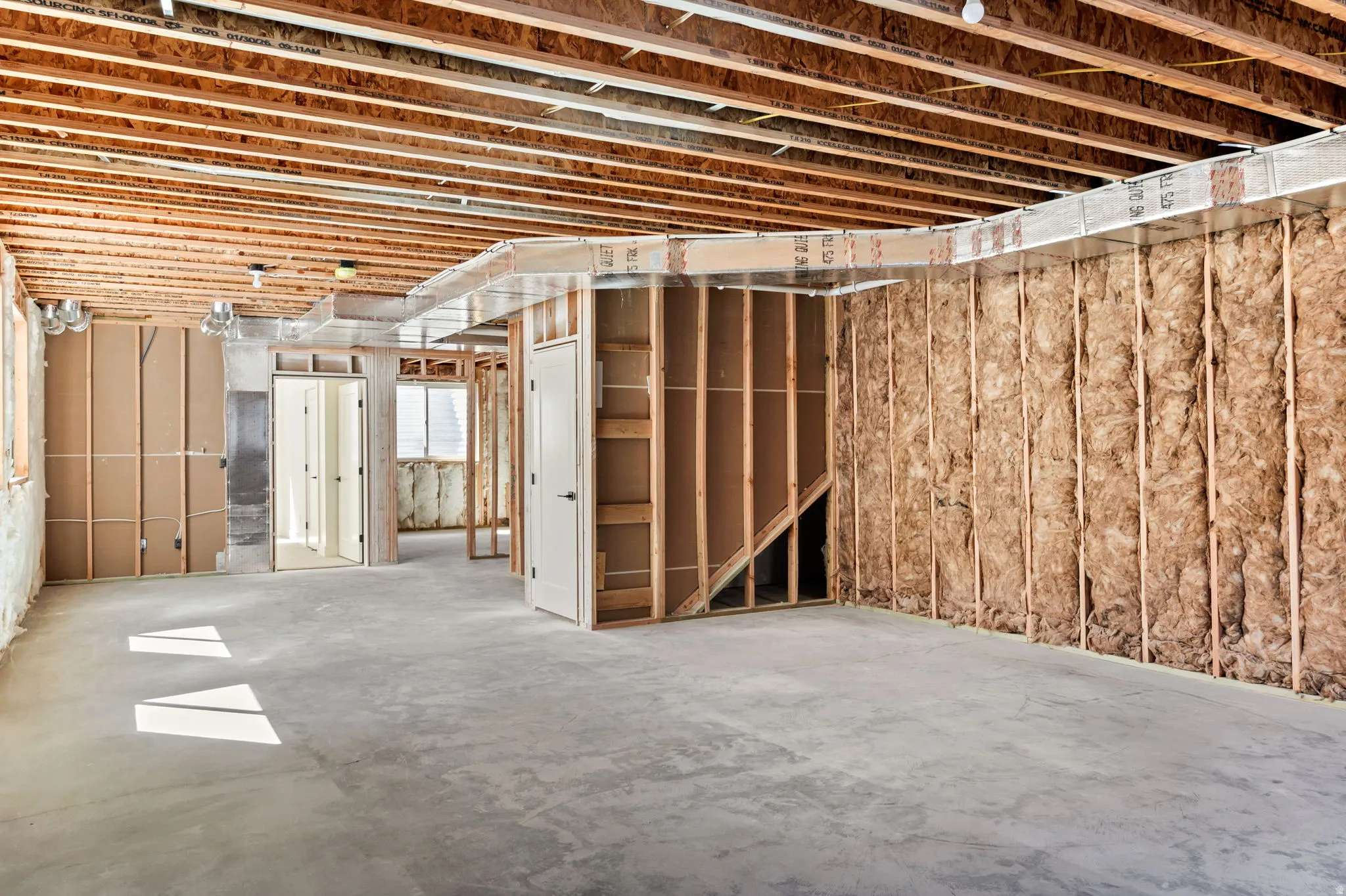 Unfinished lower level featuring exposed wood joists, concrete flooring, and insulated wall framing