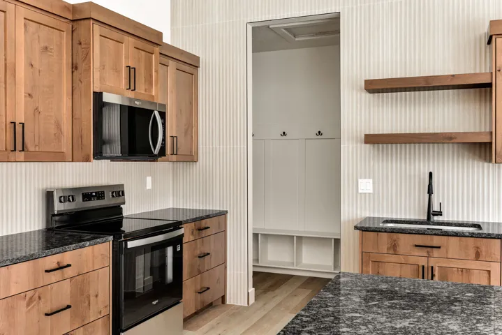 Wood-finish cabinetry and drawers, dark stone countertops, stainless steel appliances, a built-in boot bench, and wood-finish open shelving