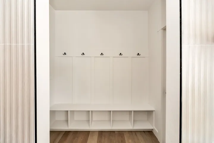 Built-in white storage bench with cubbies, five black hooks, and wood-finish flooring