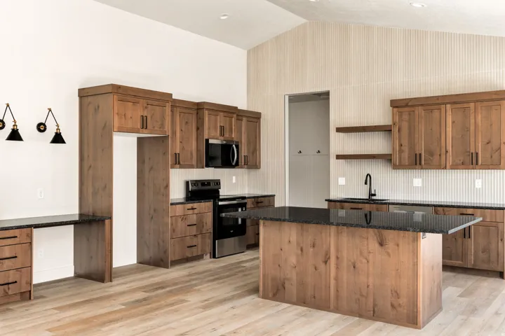 Vaulted ceiling with a white finish, wood-finish flooring, wood cabinetry with dark hardware, dark countertops, and a central island