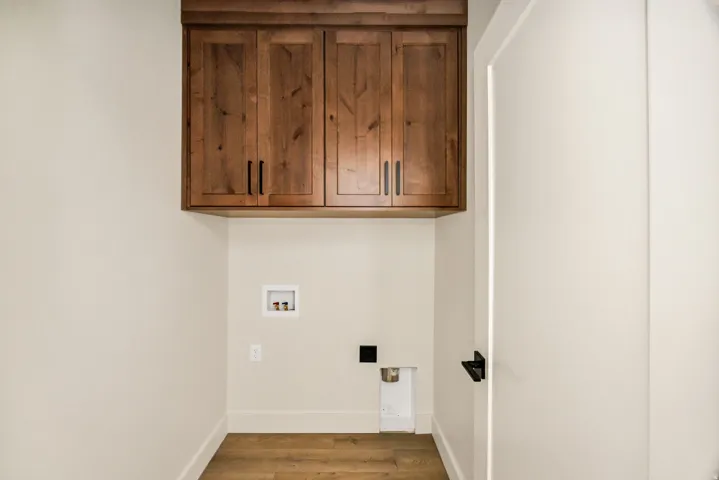 Wood-finish flooring, overhead wood cabinetry with matte black hardware, and a white interior door with matte black hardware
