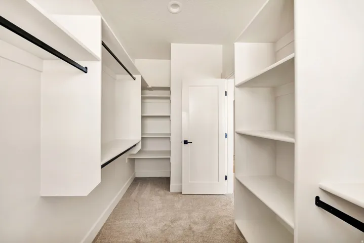 Built-in white shelving, black hanging rods, and light-colored carpeting