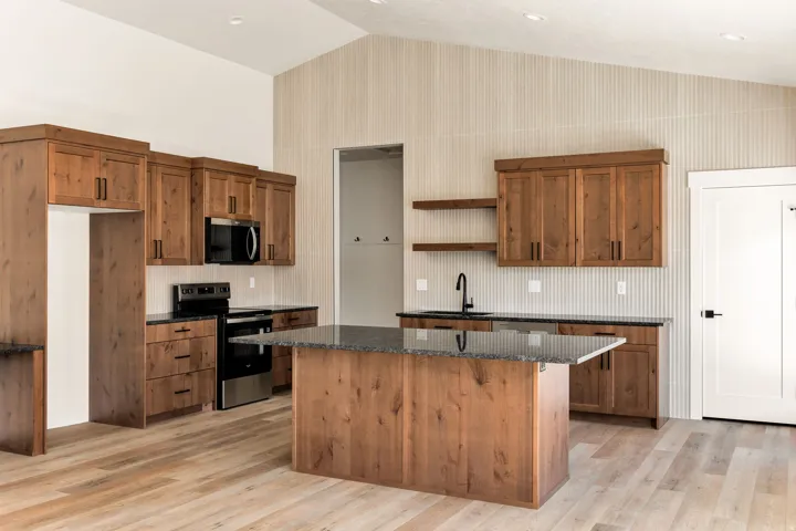 Vaulted ceiling kitchen featuring wood-finish cabinetry, a central island with a dark countertop, black appliances, and a black faucet
