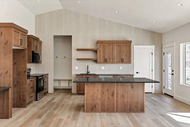 Wood-finish flooring, vaulted ceiling, wood cabinetry, dark countertops, and stainless steel appliances