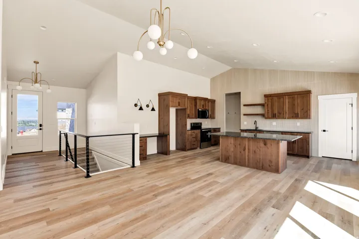 Vaulted ceilings, wood-finish flooring, contemporary lighting, wood cabinetry, and a kitchen island with stone countertop