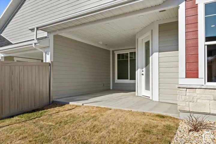 Covered patio with concrete flooring, accented with light-toned siding, stone veneer detailing, and a privacy fence