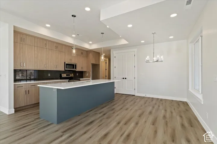 Open-concept kitchen and dining area featuring wood-finish flooring, a large island with a light-toned countertop, and stainless steel appliances