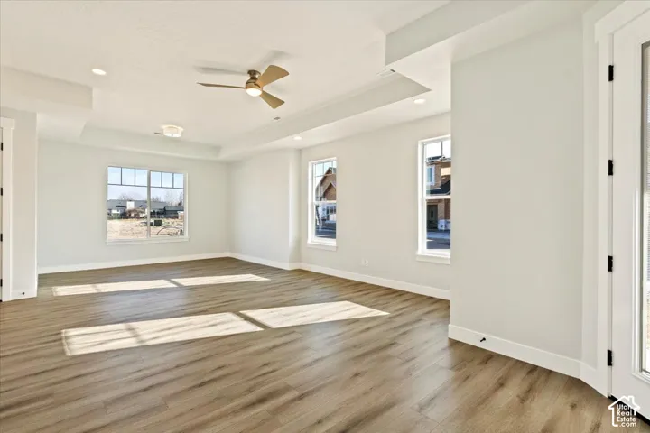 Expansive room featuring wood-finish flooring, multiple windows, a tray ceiling, recessed lighting, and a ceiling fan