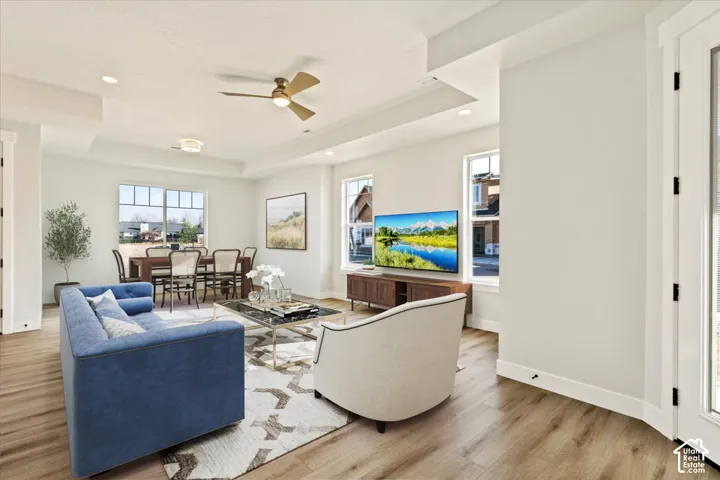 Bright open-concept living area showcasing hardwood flooring, coffered ceiling with ceiling fan, and abundant natural light from multiple windows