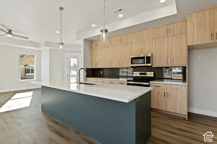 Kitchen featuring wood-finish cabinetry, dark countertop with matching backsplash, stainless steel appliances, and a central island with a white countertop
