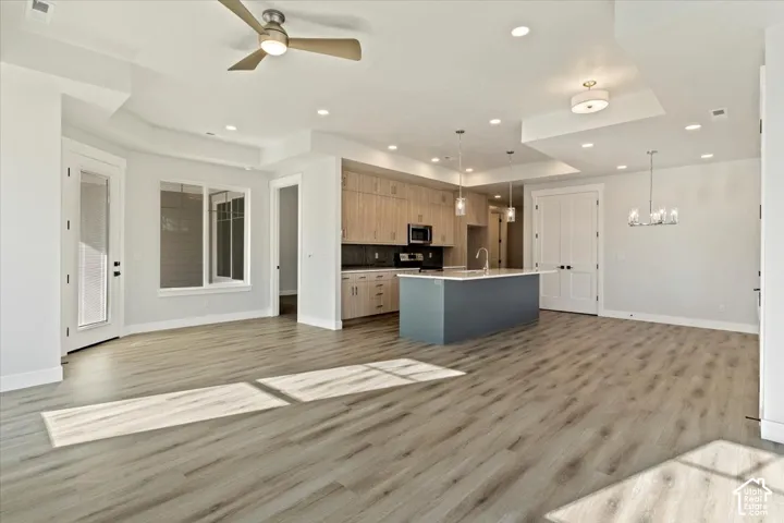 Open-concept living area featuring wood-finish flooring, recessed lighting, a ceiling fan, and a kitchen with a central island and light wood-tone cabinetry