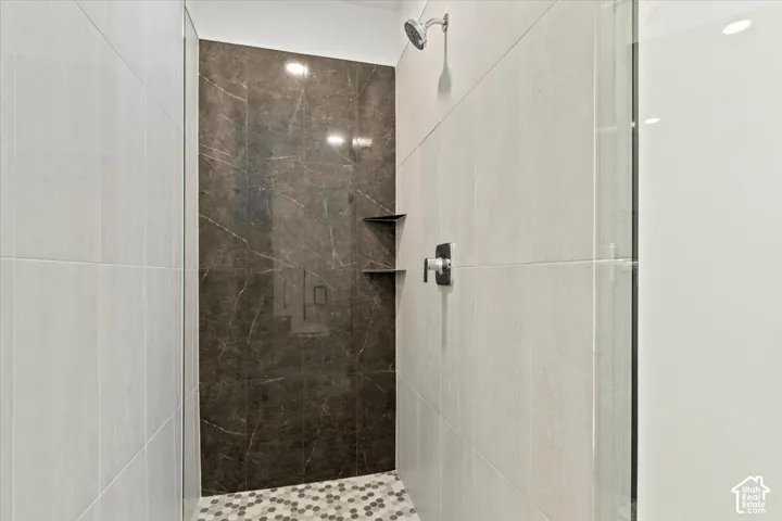 Walk-in shower with a rainfall showerhead, dark marble-finish accent wall, built-in shelving, and a hex tile floor