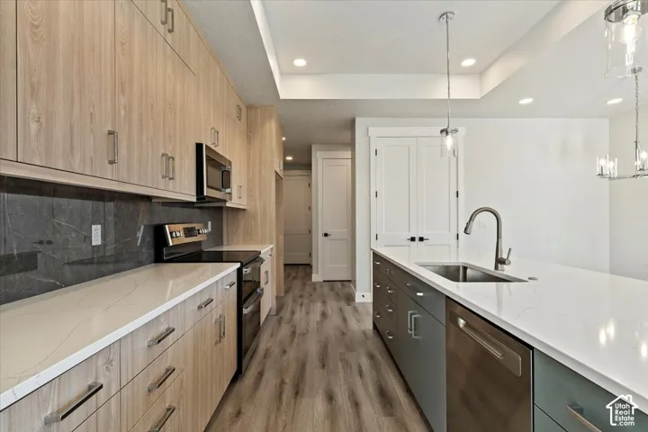 Kitchen featuring wood-finish cabinetry, stainless steel appliances, white countertops, a dark backsplash, and an island with a built-in sink and dishwasher