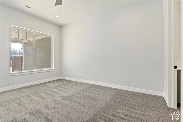 Recessed ceiling lighting, ceiling fan, large window, light gray walls, and patterned carpeting
