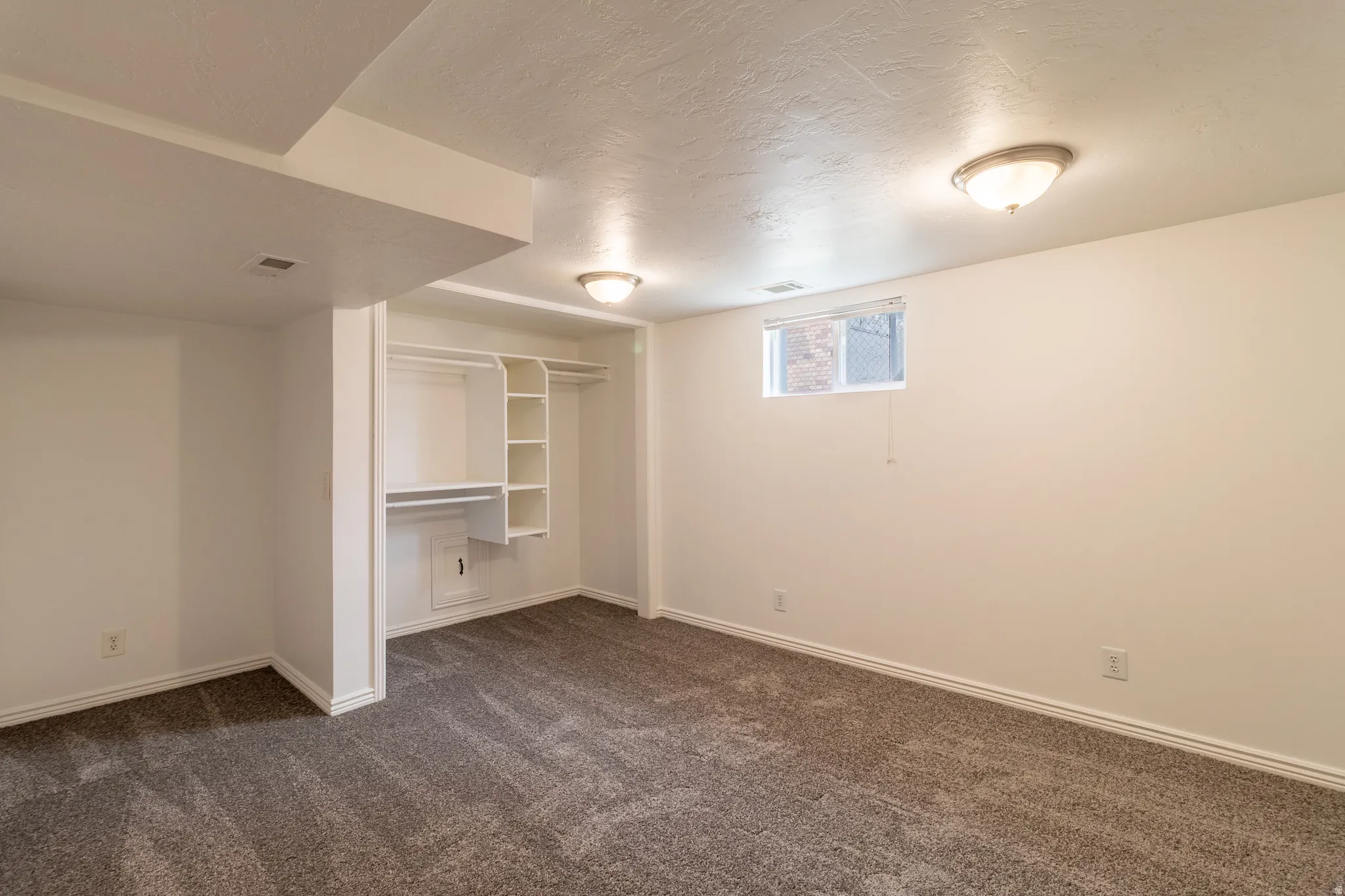 Recessed window with white trim, built-in shelving, white walls, and gray carpet flooring