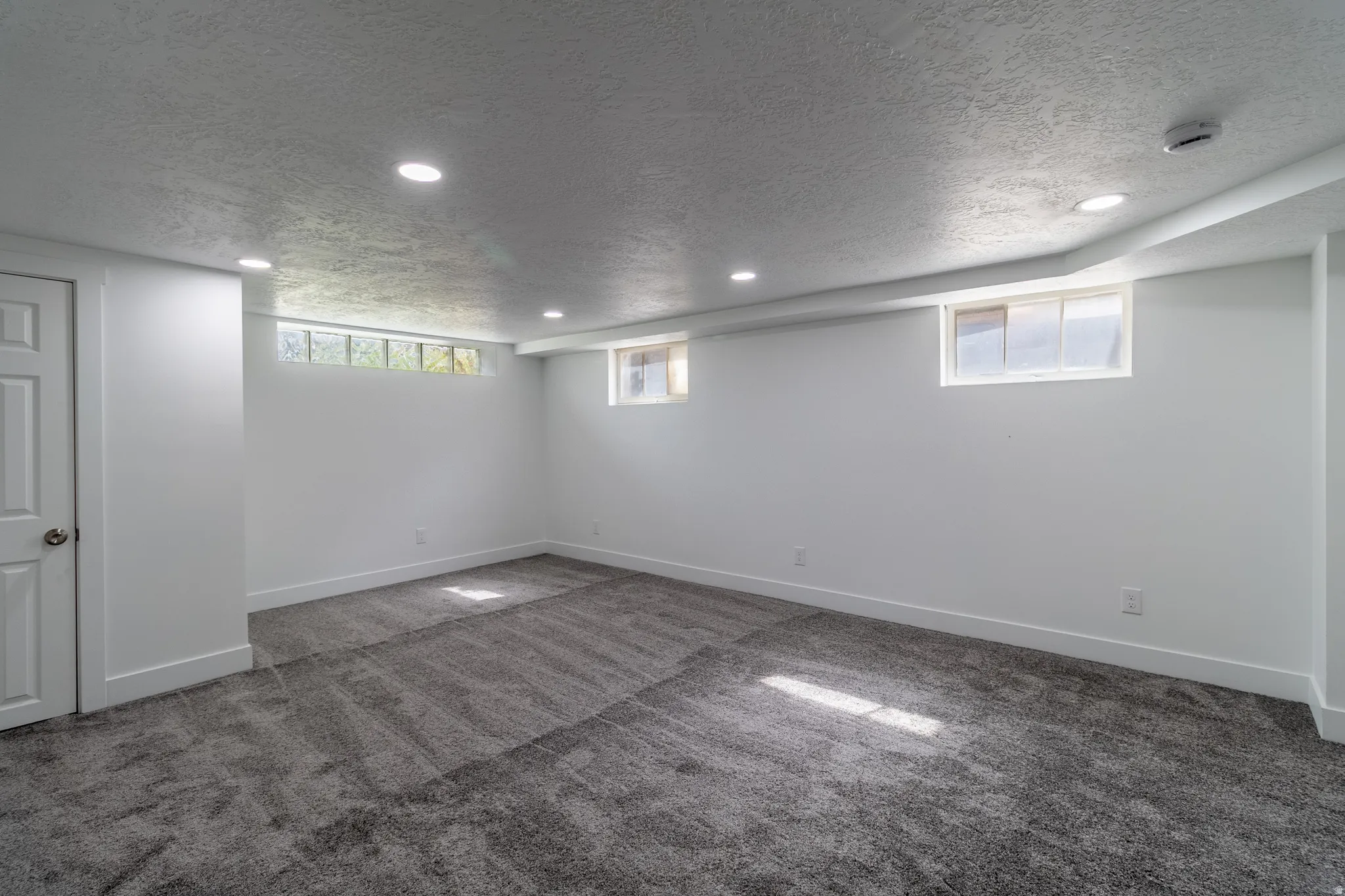 Recessed lighting, white paneled door, gray carpet flooring, white walls, and multiple windows