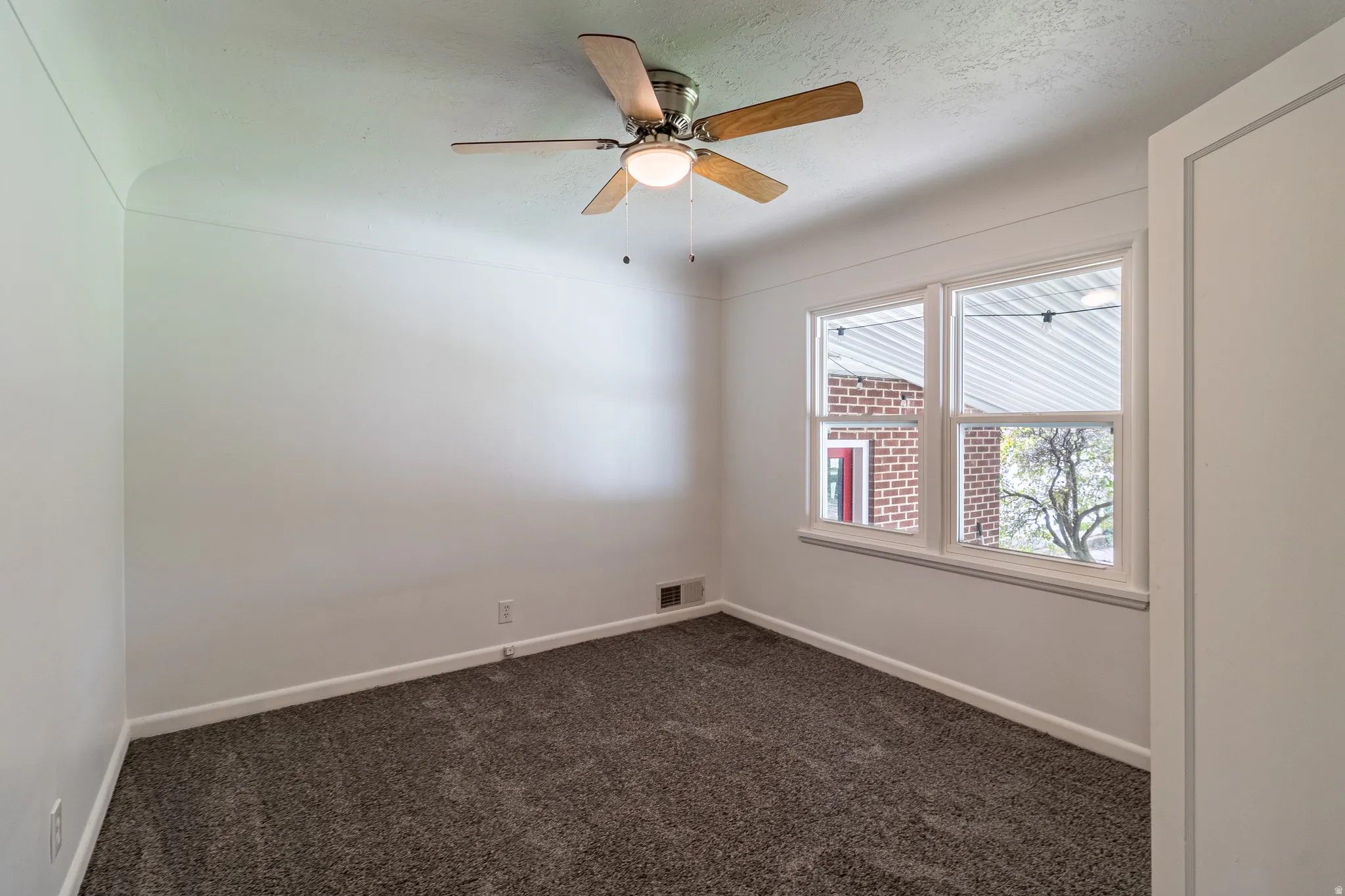 Textured carpeting, white painted walls, a ceiling fan with light fixture, and two paneled windows