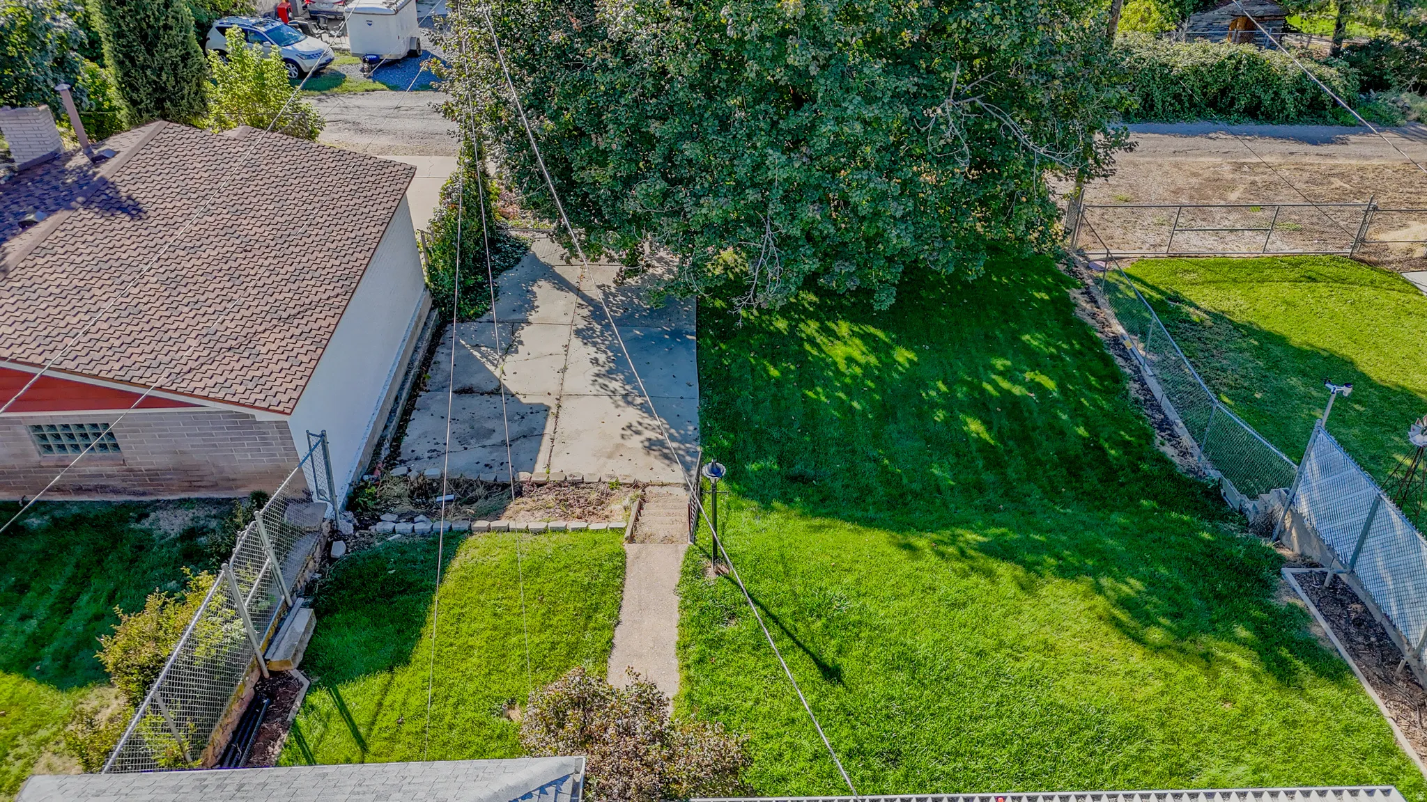 Gabled roof with terra cotta tiles, brick exterior, fenced yard, concrete driveway, and mature trees