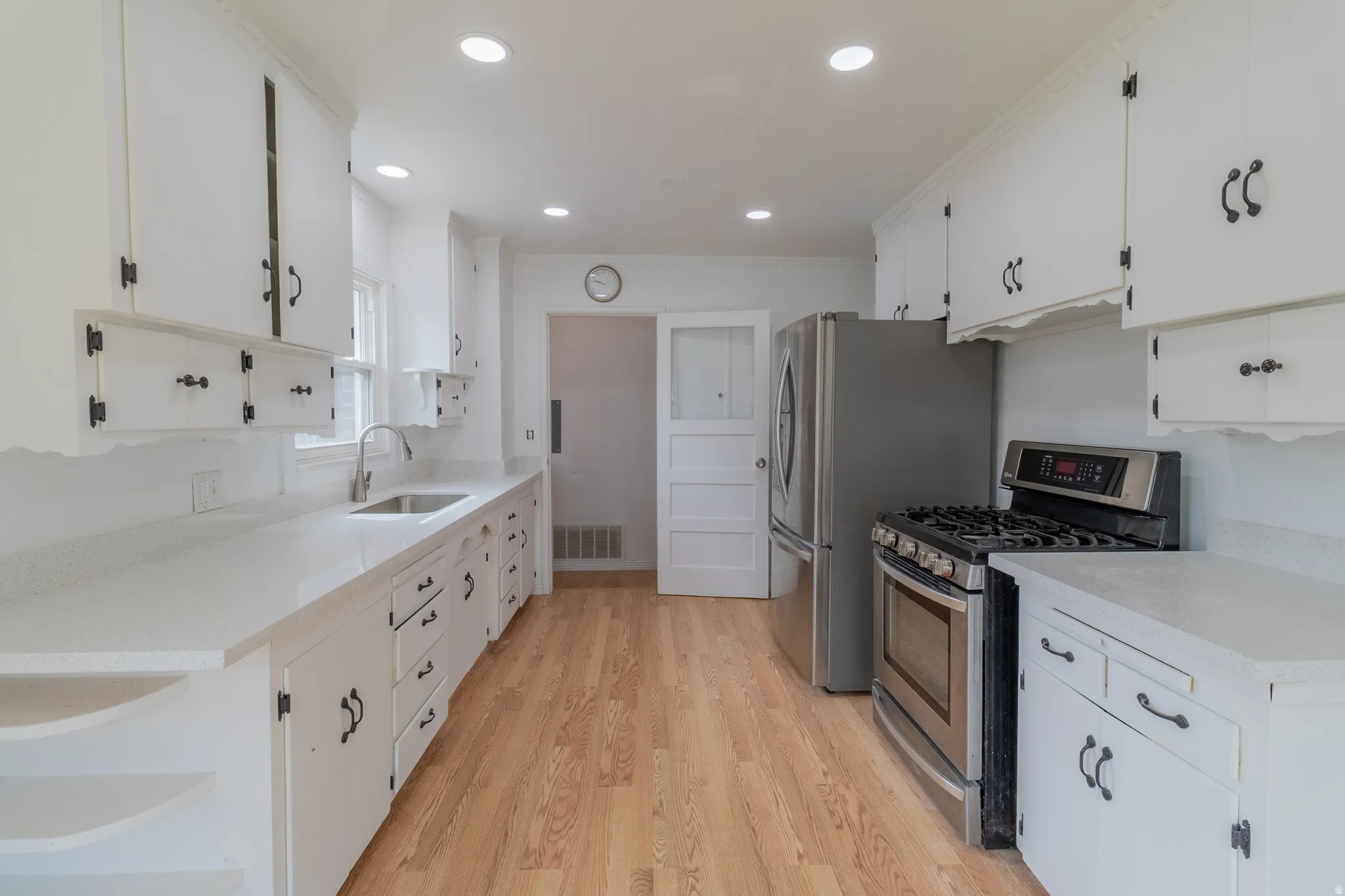 White cabinetry with black hardware, light-toned wood-finish flooring, recessed lighting, and a stainless steel gas range