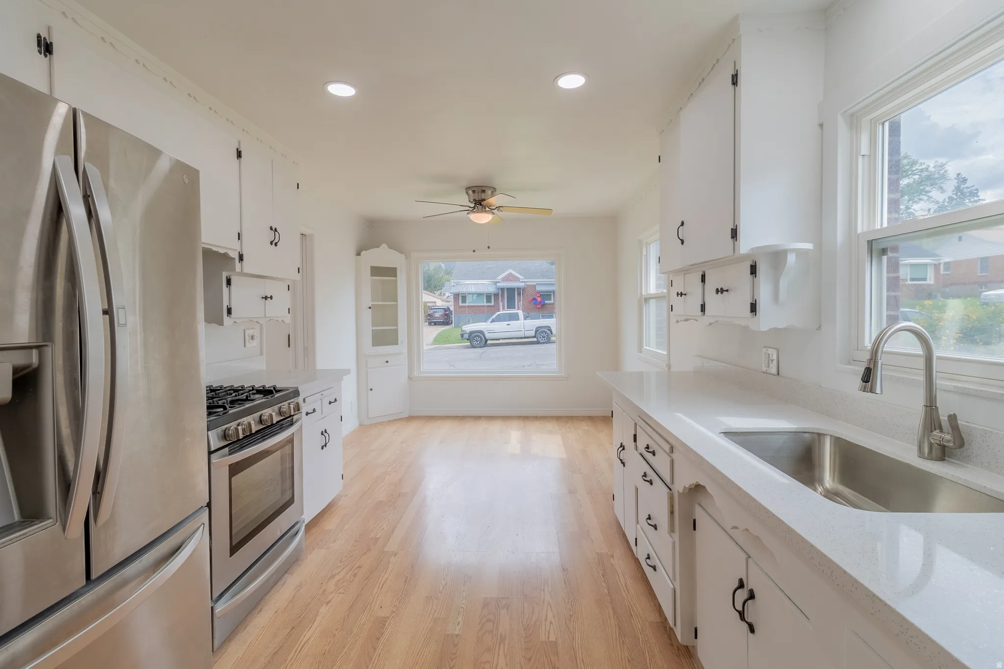 Open-concept kitchen featuring stainless steel appliances, white cabinetry, light countertops, and wood-finish flooring