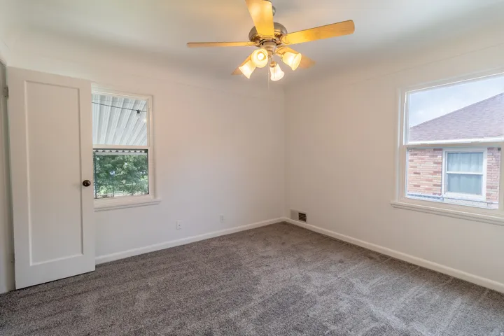 Neutral wall paint, ceiling fan with light fixture, gray patterned carpeting, and white window trim