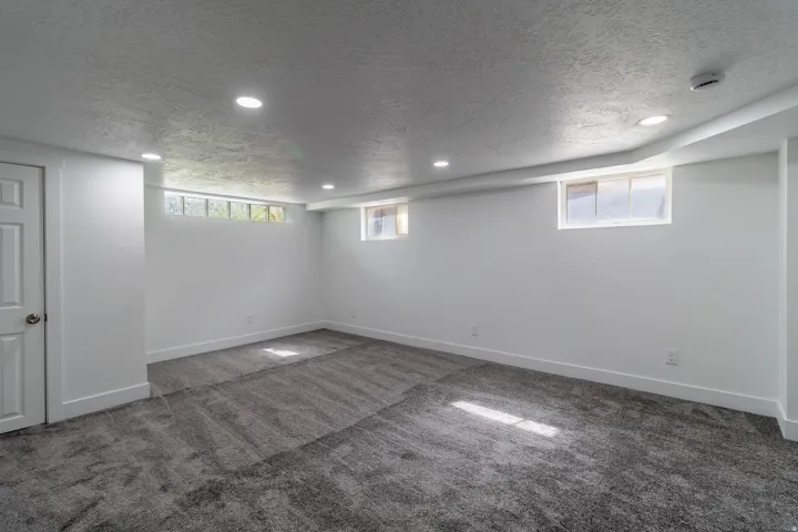 Recessed lighting, white paneled door, gray carpet flooring, white walls, and multiple windows