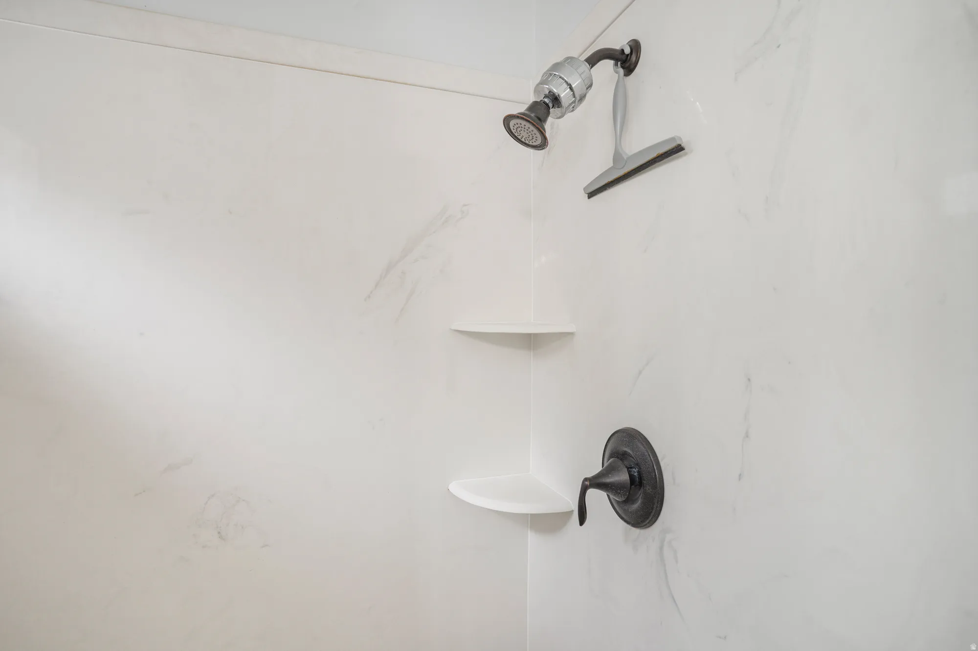 Shower featuring white stone-finish walls, a dark-finish shower head, and built-in corner shelving
