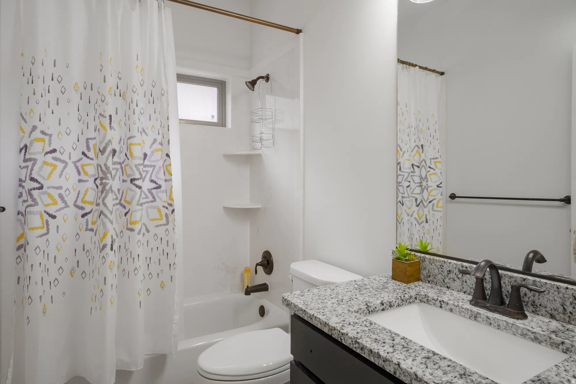Bathroom featuring a white bathtub, built-in shelving, a shower head with a handheld sprayer, a dark vanity, and a light-colored speckled countertop